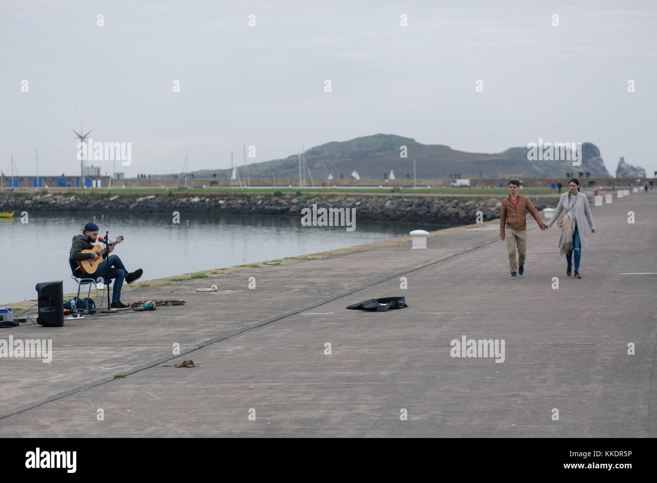 Man busking on a Howth`s pier playing and singing romantic songs to passing by tourists. Howth Peninsula with Ireland`s Eye, Dublin, Ireland Stock Photo